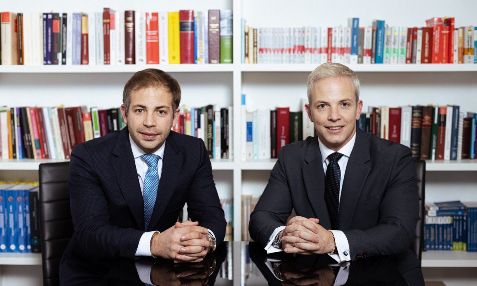 Los dos socios del despacho sentados ante la biblioteca jurídica